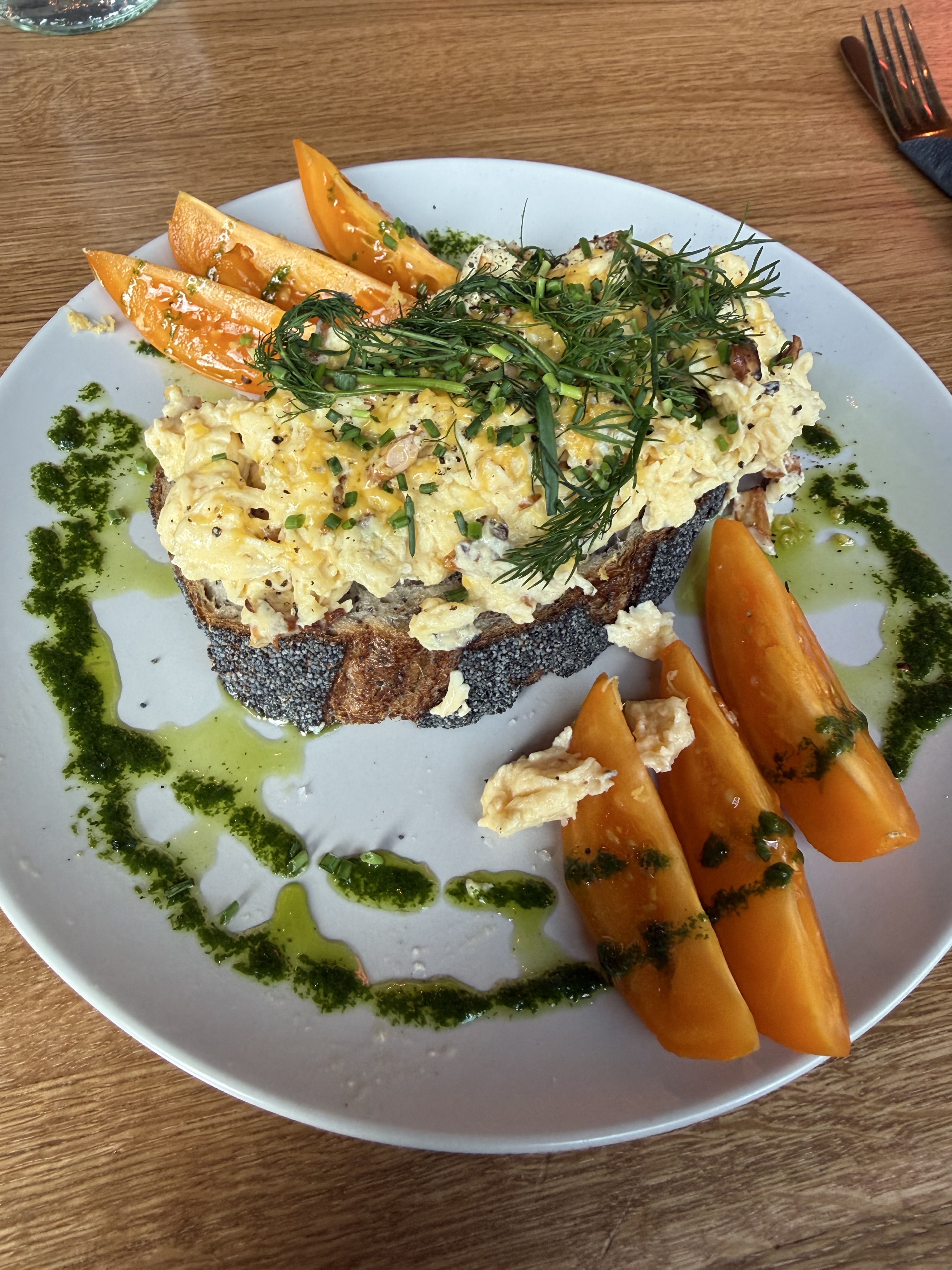 Breakfast on 2026-08-28: open toast topped with scrambled eggs, dill, and chives, with orange tomato wedges and green herb oil
